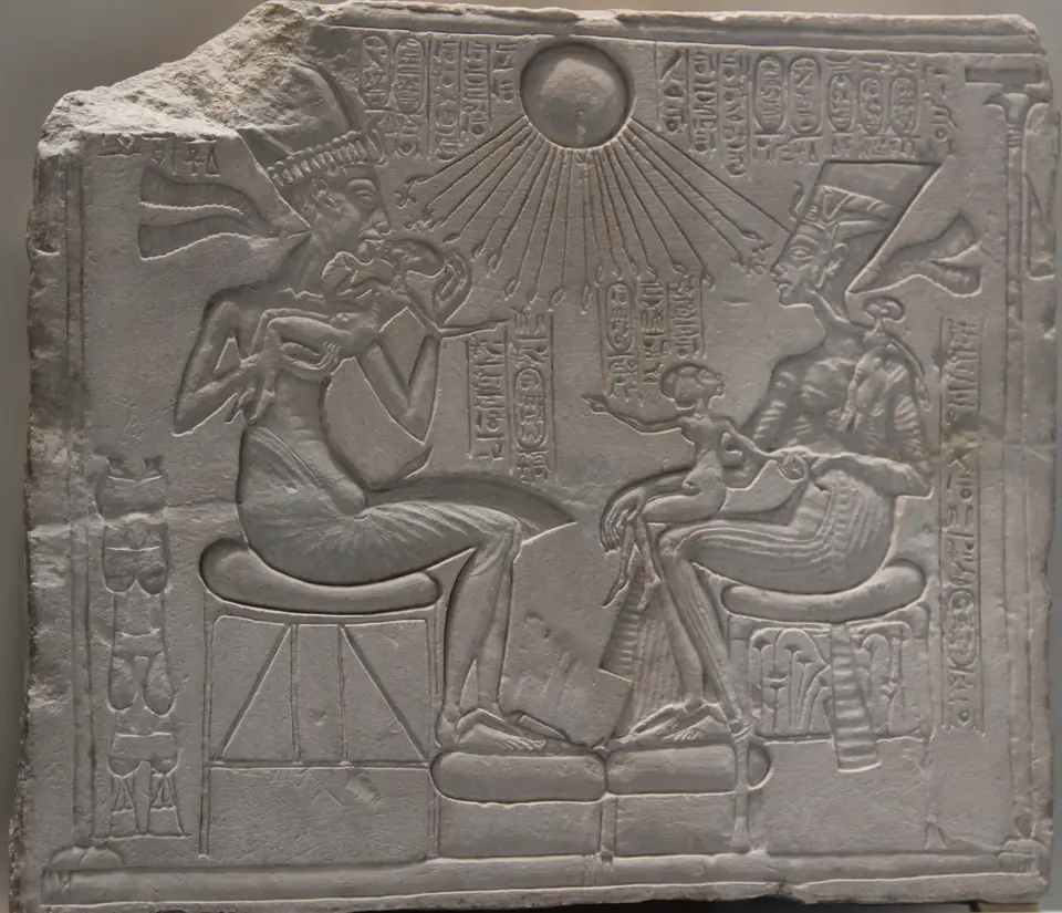 A limestone relief of a king and queen seated facing each other, holding small children, under a sun disk whose rays end in hands.