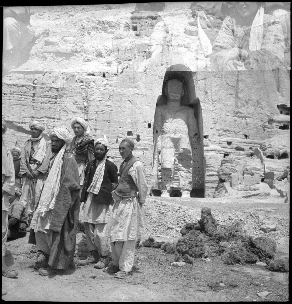 Men standing in front of a cliff with a giant standing figure carved inside a deep arched niche, in an old photograph.