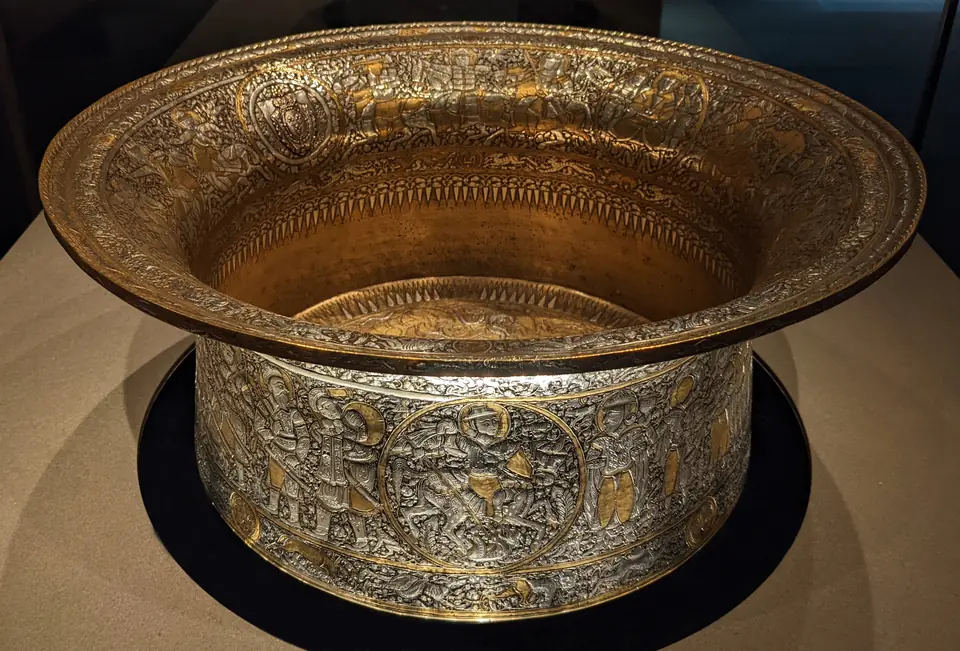 A large brass basin decorated with bands of figures inlaid with silver and gold.