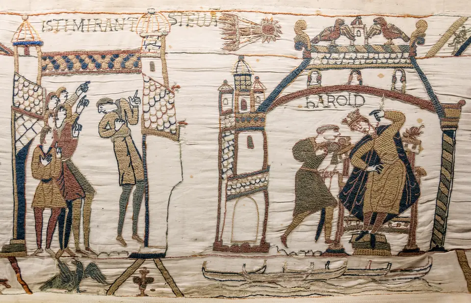 A section of a long embroidered strip showing a comet in the sky, men pointing up at it and a crowned king on a throne, with words stitched above.