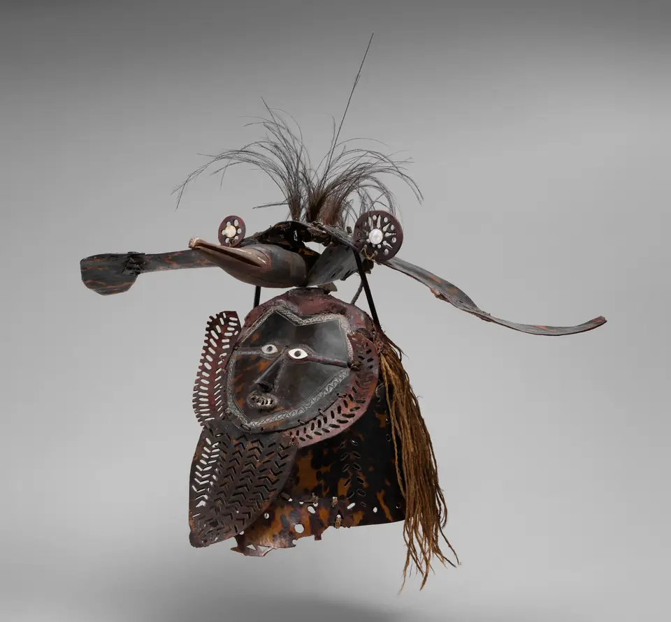 A mask of turtle shell plates shaped like a face combined with a bird form, trimmed with feathers and fiber.