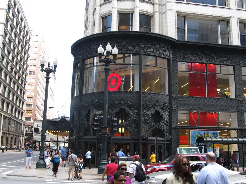 A white multistory building with wide windows in a grid and an ornate dark metal corner entrance.