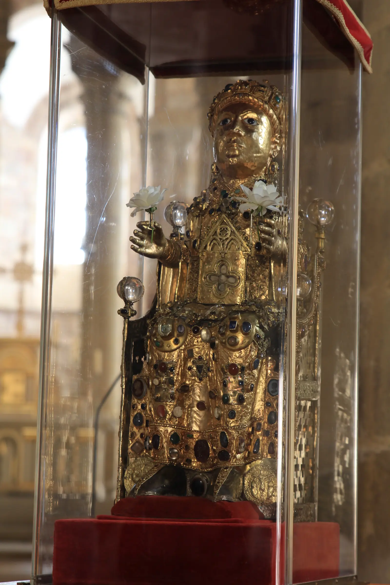 A small seated figure covered in gold, with a large staring face, set with gems and crystals.