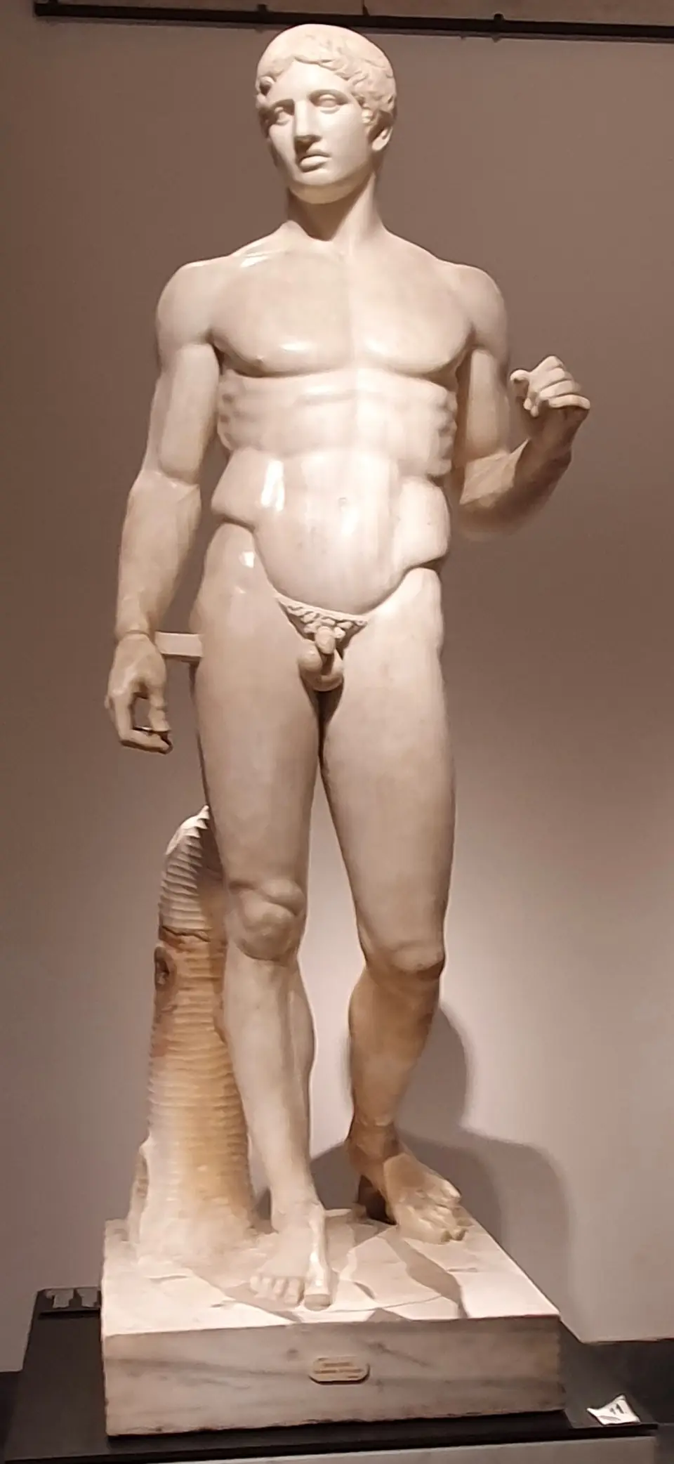 A marble statue of a nude muscular man, his weight on one leg and his head turned slightly.