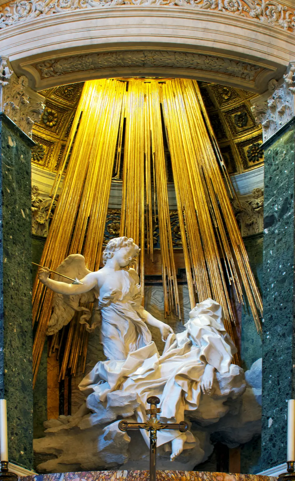 A marble sculpture of a swooning woman on a cloud while a smiling winged youth holds an arrow over her, with gilded rays behind.