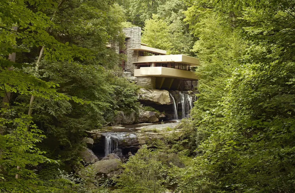 A house of concrete terraces and stone cantilevered over a waterfall in a wooded valley.