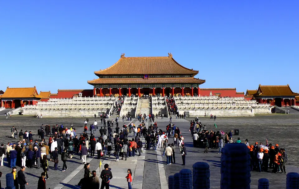 A large palace hall with a double golden roof on a white marble platform, with crowds in a huge courtyard.