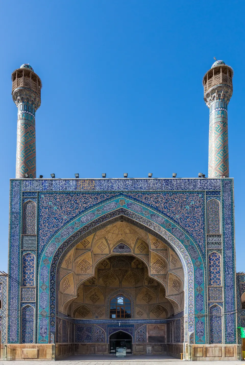 A tall courtyard entrance framed by a huge arched porch covered in blue tilework, with two minarets.