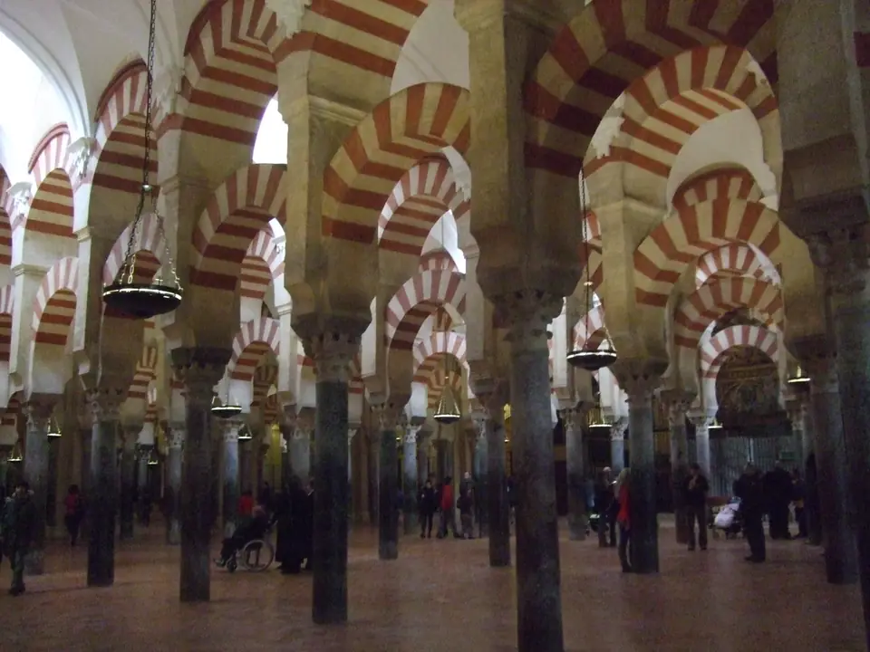 A dim hall filled with rows of slender columns supporting two tiers of arches striped in red and white.