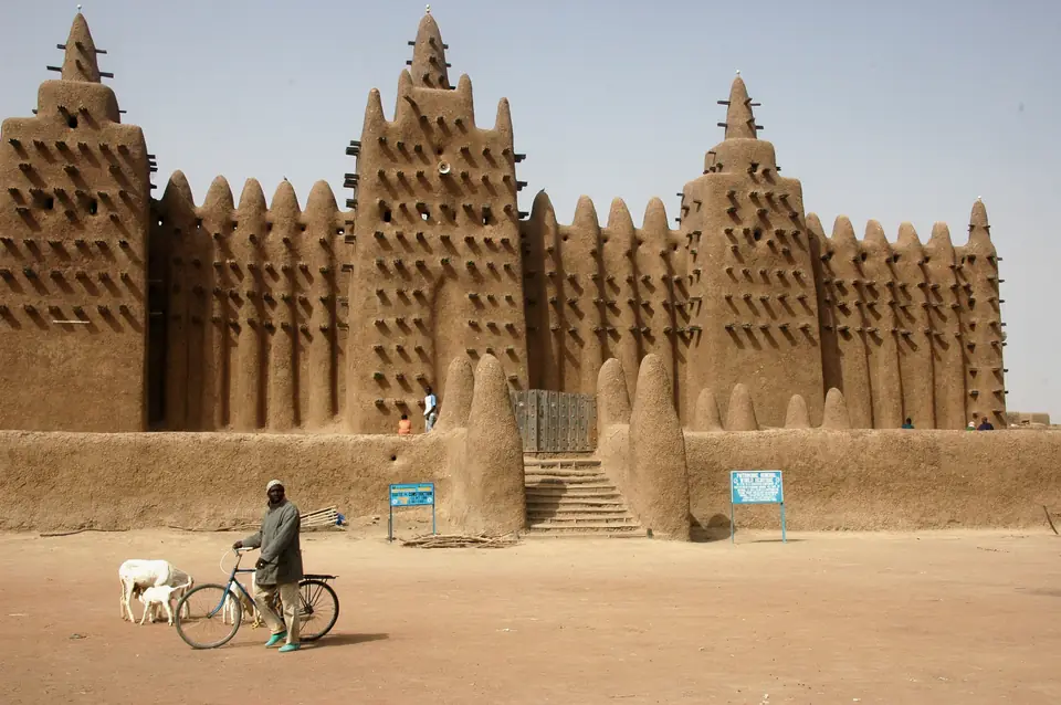 A huge mud-brick building with towers topped by cones and wooden beams sticking out of the walls.