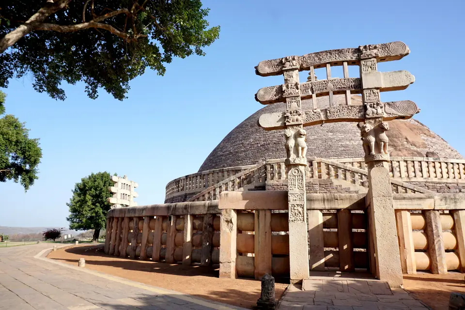 A large hemispherical stone dome with a railing around it and a tall carved stone gateway in front.