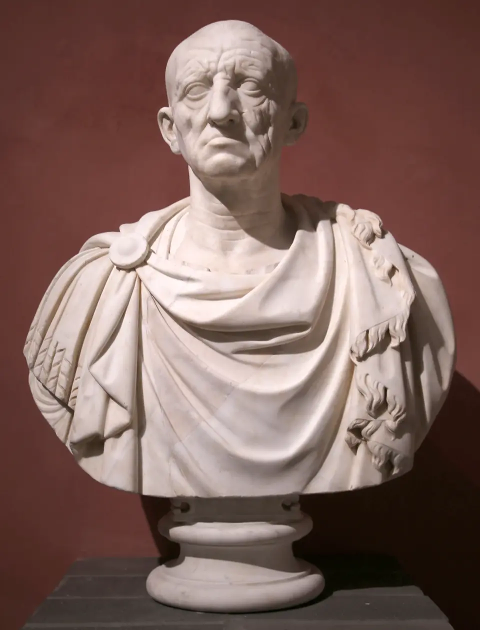 A marble portrait of an old man with a deeply wrinkled face, sunken cheeks and a tight mouth, set on a draped bust.