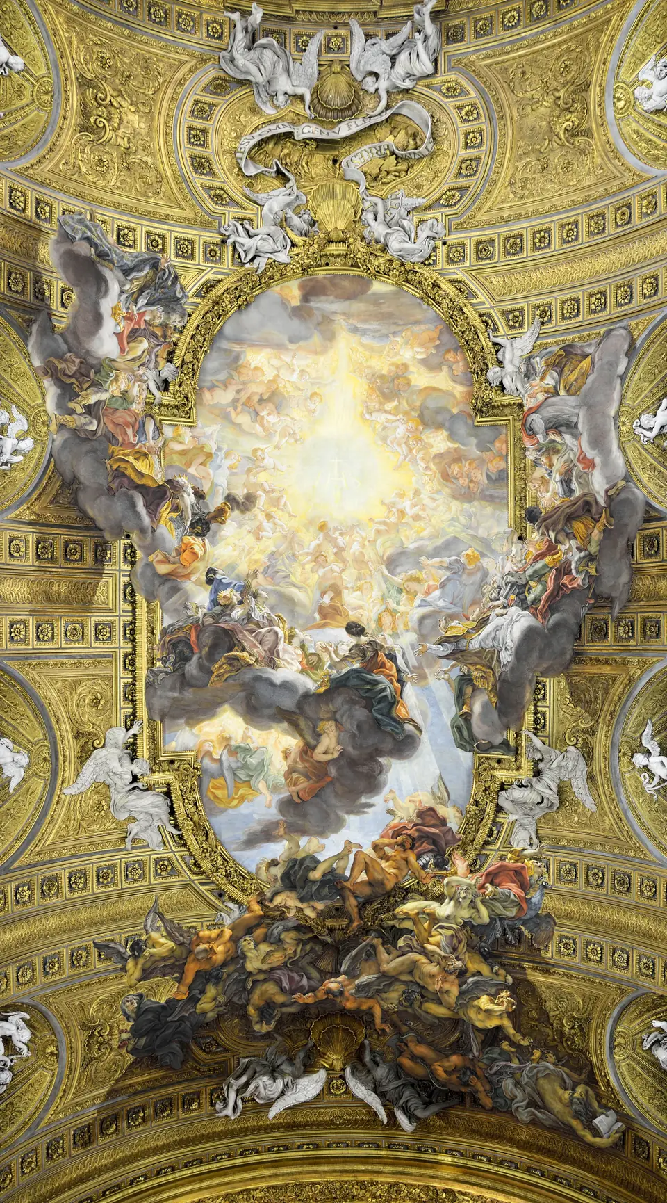 Looking straight up at a church ceiling: a golden glow at the center of a painted sky, surrounded by swirling clouds and figures that spill over a gilded frame onto the coffered gold vault, with white stucco angels around the edges.