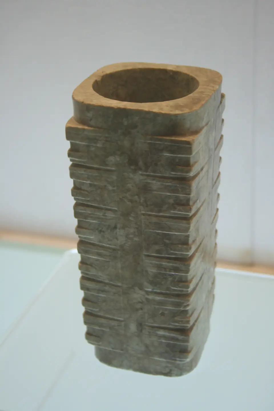 A tall, square jade tube with a round opening at the top, its sides cut into stacked horizontal bands.