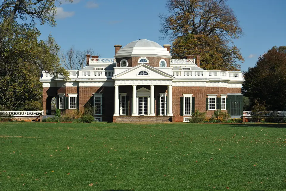 A brick house with a white columned portico and a low dome, set behind a lawn.