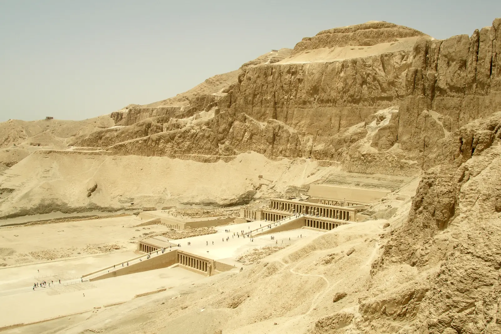 A temple of three long colonnaded terraces connected by ramps, set against a steep rocky cliff.