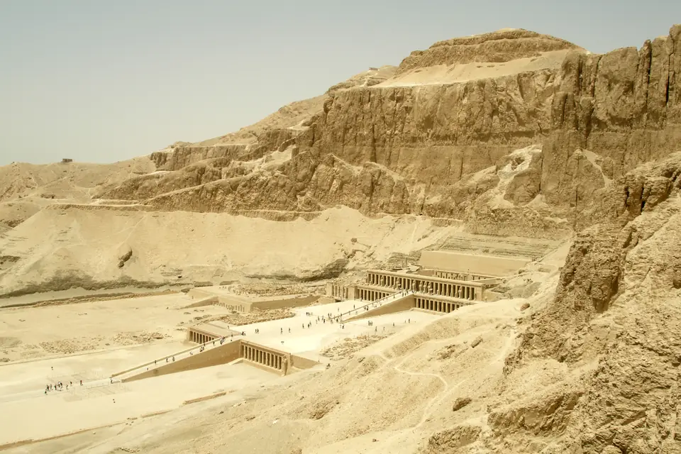 A temple of three long colonnaded terraces connected by ramps, set against a steep rocky cliff.