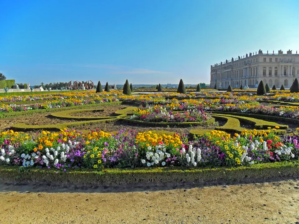 Formal gardens of patterned flower beds, with a long stone palace facade in the distance.
