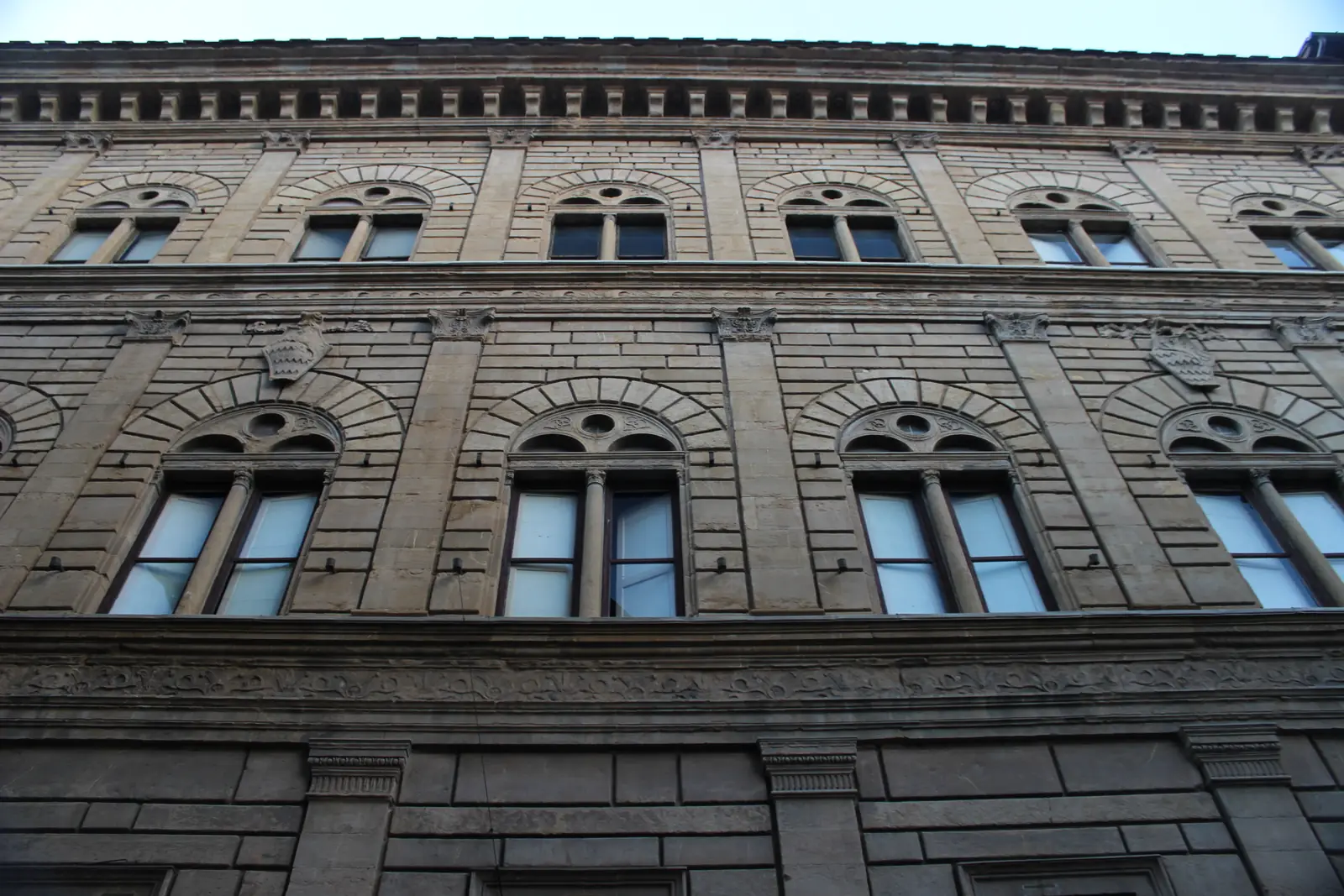 A three-story stone palace facade divided by flat pilasters and horizontal bands, with paired arched windows.