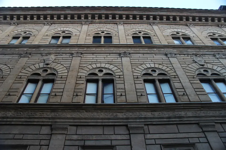 A three-story stone palace facade divided by flat pilasters and horizontal bands, with paired arched windows.