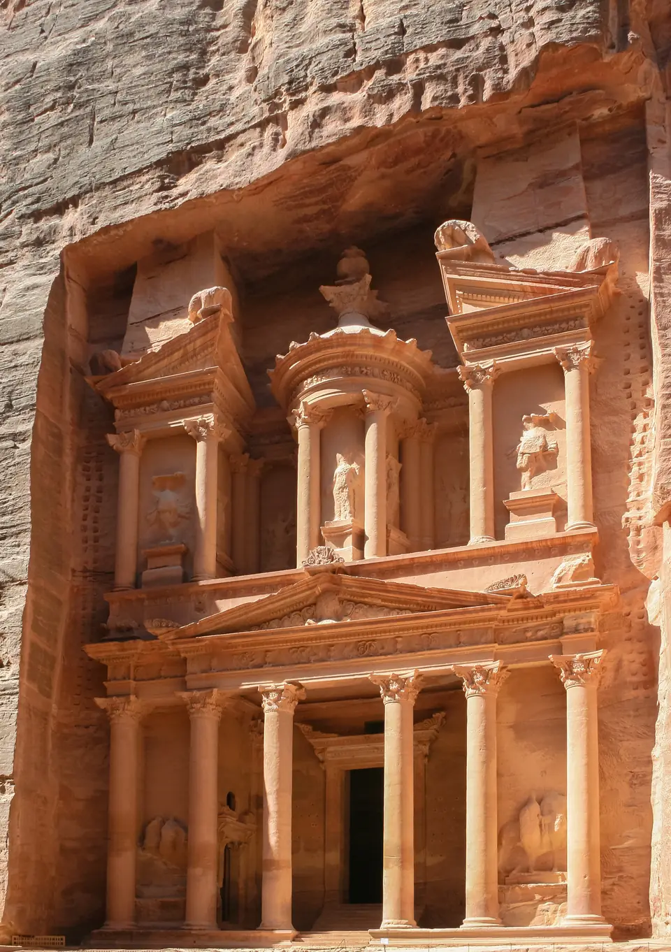 A tall temple facade with columns and statues carved directly into a rose-colored cliff.