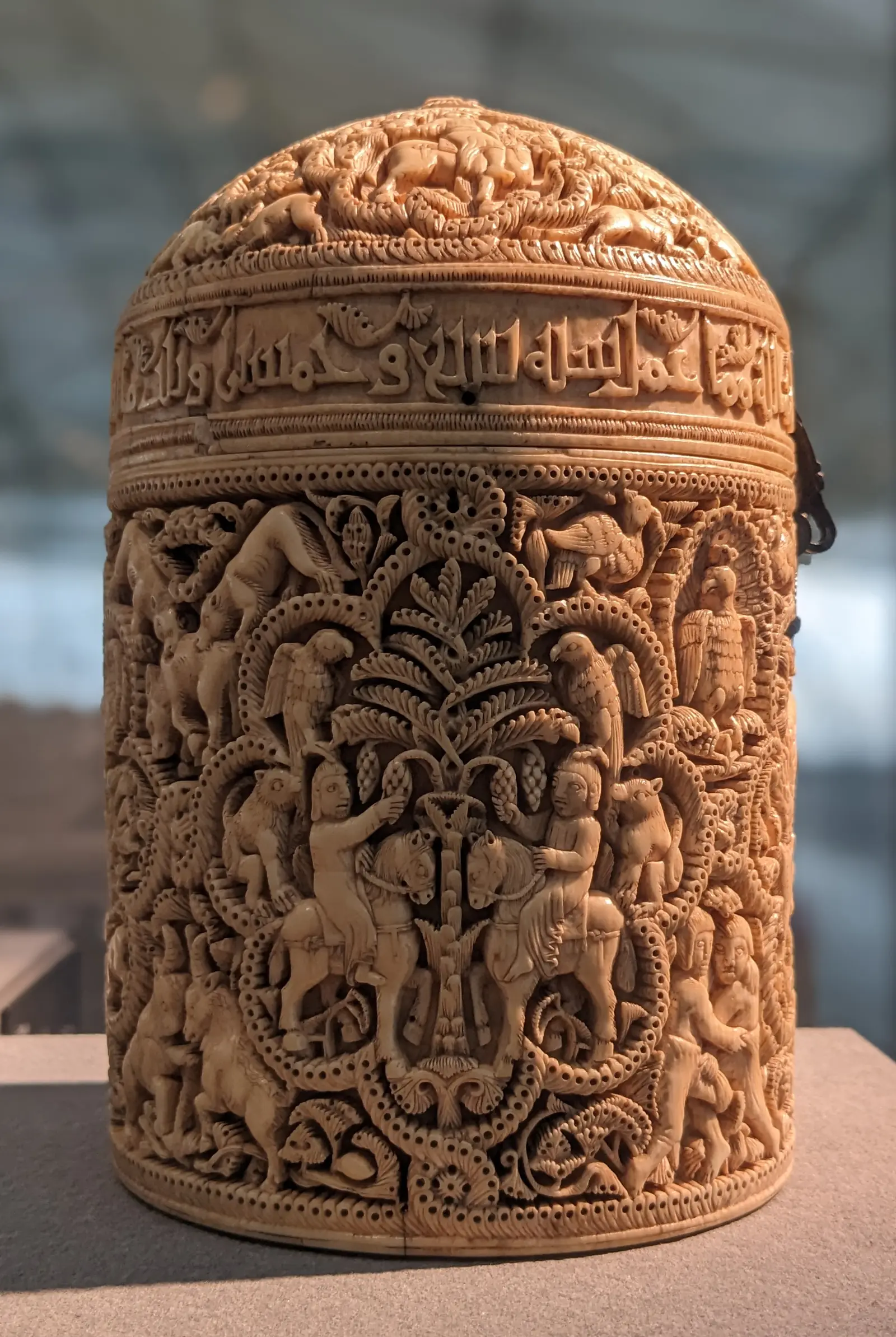 A small, round ivory box with a domed lid, carved all over with figures and animals in lobed medallions among vines.