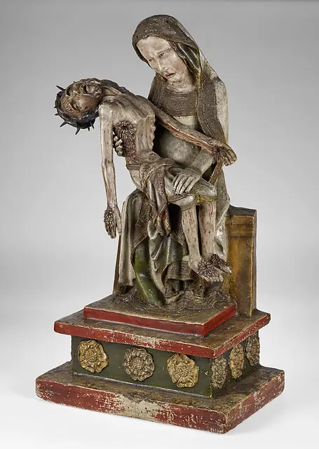 A painted wooden sculpture of a grieving woman holding a thin, stiff dead man with bloody wounds across her lap.