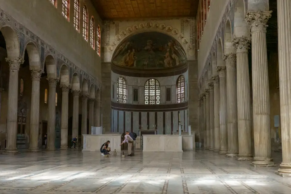 A long, bright church interior with rows of white columns supporting arches, large windows high in the walls and a rounded apse at the end.