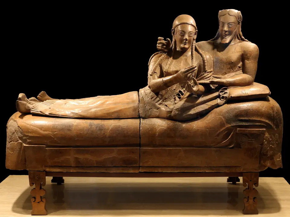 A terracotta coffin lid with a smiling man and woman reclining together as if at a banquet.