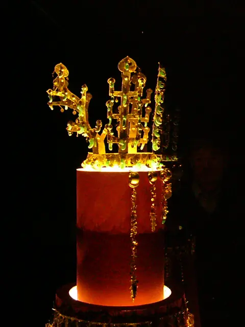 A tall gold crown with branch-like and antler-like uprights hung with jade pieces, displayed in a dark case.