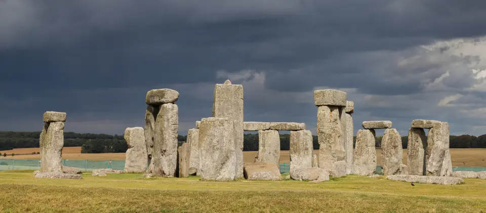 A ring of massive standing stones, some topped by horizontal stones, on an open grassy plain.