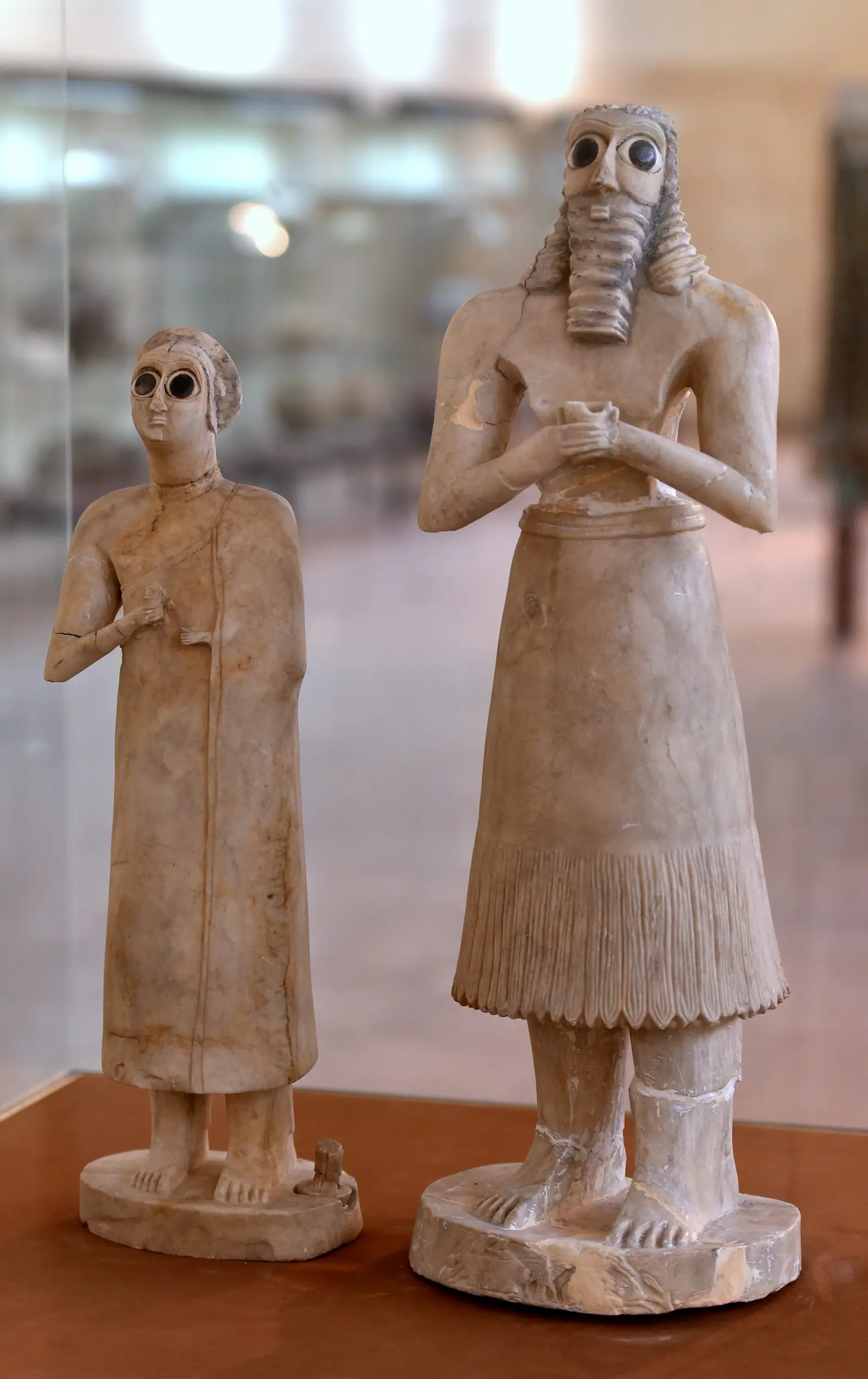Two standing stone figures, one bearded, with huge inlaid eyes and hands clasped at their chests.