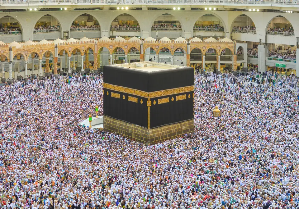 A large black cube covered in cloth with a gold-embroidered band, surrounded by a dense crowd of pilgrims.