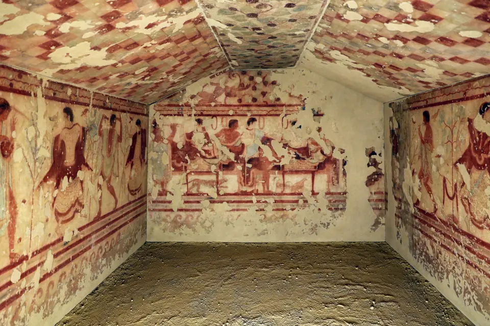 A painted tomb chamber: figures recline at a banquet on the back wall, and dancers and musicians appear on the side walls.