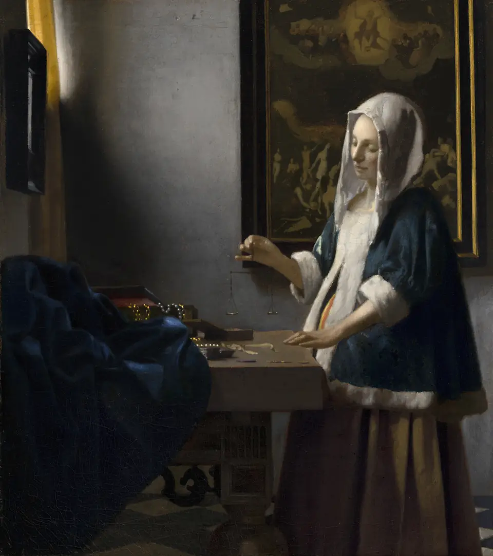 A woman in a blue jacket stands at a table holding small scales, lit by a window at left, with a painting on the wall behind her.