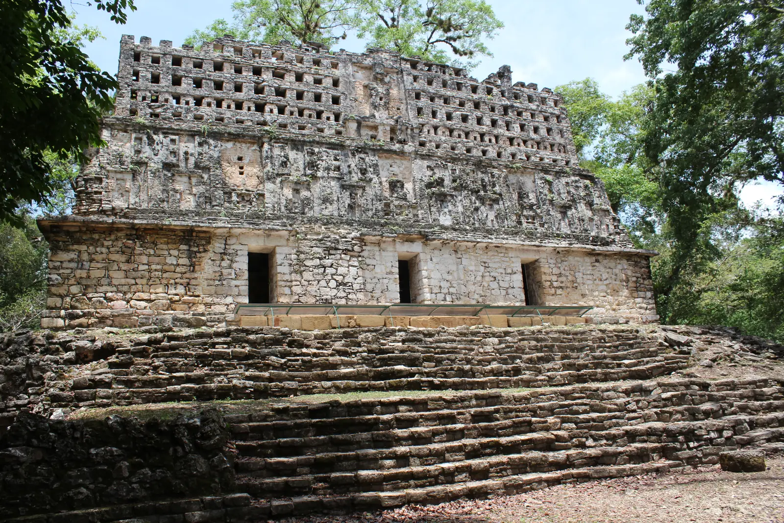 A stone temple on a terrace with doorways and a tall, openwork crest on its roof, surrounded by forest.